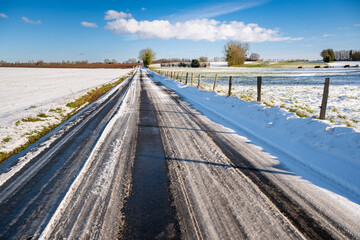 Wall Mural - Paysage d'hiver. Route de campagne enneigée avec verglas à travers prairies et champs