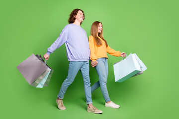 Sticker - Full length profile portrait of two youngsters hold arms store bags walk empty space isolated on green color background