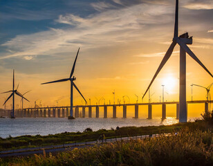 Wall Mural - wind turbines at sunset with a bridge in the background