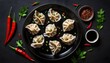 Asian dumplings with soy sauce, chili peppers and herbs on a dark background top view