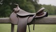 A classic, brown leather saddle resting on a fence