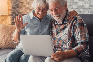 Wall Mural - Cute couple of old people sitting on the sofa using laptop together shopping and surfing the net. Two mature people in the living room enjoying technology talking in video call with friends or family