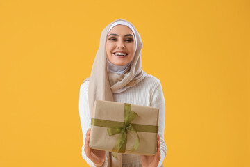 Canvas Print - Young Muslim woman with gift on yellow background. Islamic New Year celebration