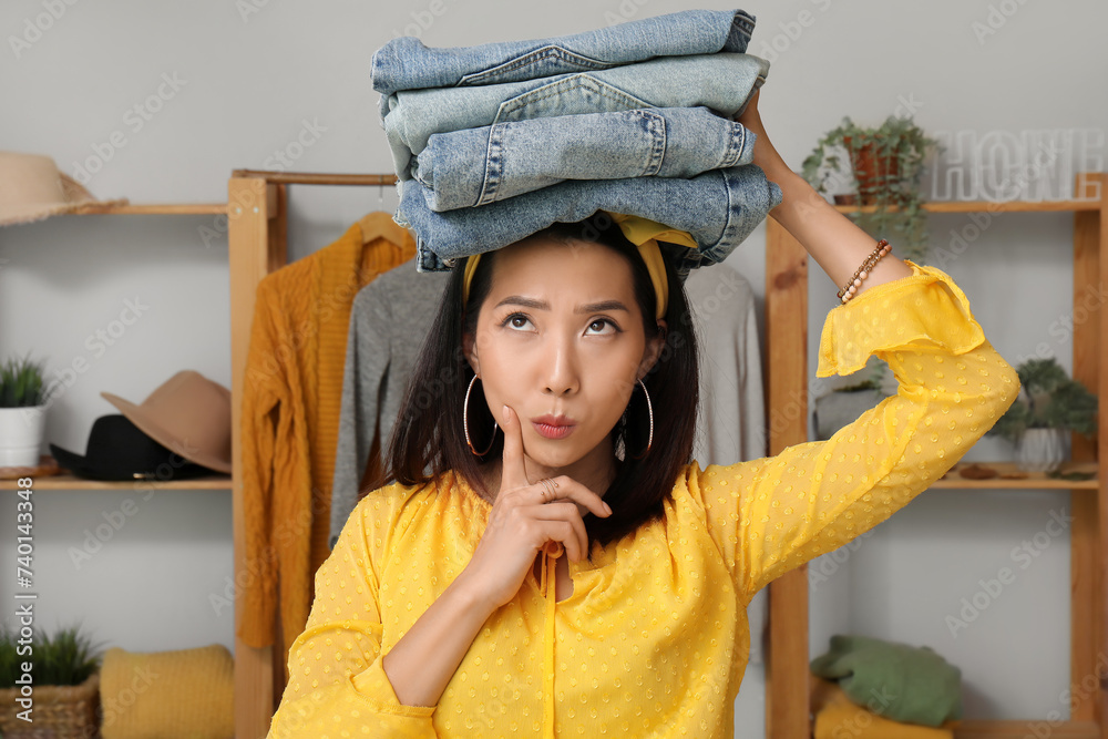 Thoughtful young woman with stack of clean clothes in laundry room
