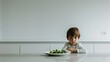 a sulking child seated in front of a plate of vegetables on a modern kitchen table, portraying the challenges of mealtime struggles and healthy eating habits in a contemporary setting.