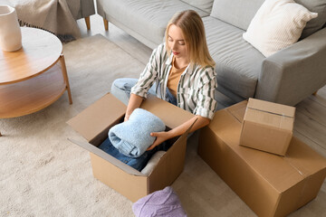 Poster - Young woman putting folded sweater in box at home