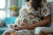 © Sergio - Close up pregnant woman is sitting in a chair with her hands resting gently on her belly. She appears to be in a hospital waiting area, patiently awaiting her turn