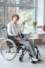 Sticker - Young businesswoman in wheelchair with laptop and mobile phone at office