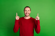 Photo of satisfied toothy beaming man with stubble dressed red pullover indicating at offer empty space isolated on green color background