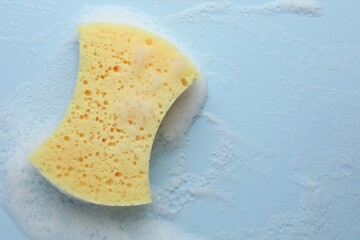 Canvas Print - Yellow sponge with foam on light blue background, top view. Space for text