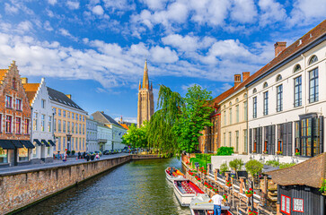 Bruges cityscape, Roman Catholic Church of Our Lady, Dijver water canal with promenade embankment, boat near wharf and medieval buildings, Brugge old town, Bruges city centre, Flemish Region, Belgium