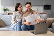 © Prostock-studio - Smiling european couple with coffee and documents near laptop