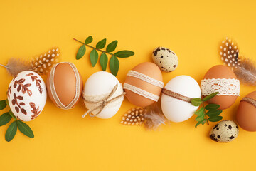 Wall Mural - Decorated Easter eggs, feathers and leaves on yellow background