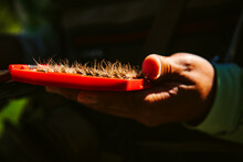 A Closeup Of A Man's Hand Holding An Open Red Box Of Furry Fishing Flies In The Sunlight Against Dark Shadows