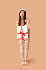 Sticker - Beautiful young woman in silky pajamas and Santa hat with Christmas gift box on brown background