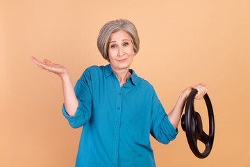 Sticker - Portrait of senior clueless pensioner person wear stylish shirt hold steering wheel shrug shoulders isolated on beige color background