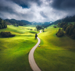 Wall Mural - aerial view of country road in green alpine meadows on overcast summer day. top view of rural road, 