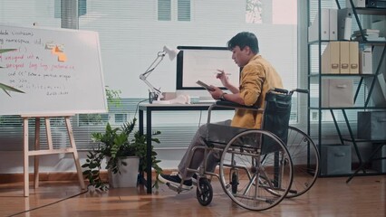 Long shot, back view of pensive male coder in wheelchair working on computer at office desk