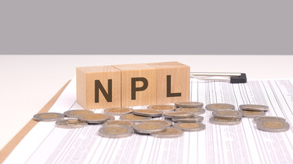 Sticker - the combination of wooden cubes spelling NPL with coins emphasizes the concept of Non Performing Loans, highlighting the financial risk and potential losses incurred