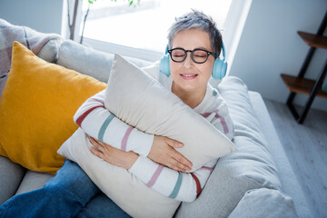 Wall Mural - Portrait of peaceful lovely person sit sofa closed eyes enjoy music headphones hands hold comfy cushion free time indoors