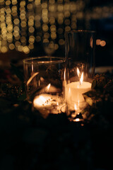 Large white voluminous candles stand on the floor at a wedding ceremony in blue evening light. Warm candlelight. Warm light, cold shadows. Shiny glass. Candles are lit in elegant glass vases on the fl