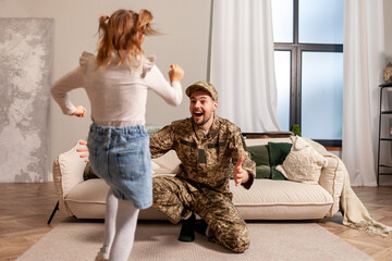 Wall Mural - happy Ukrainian army soldier in camouflage uniform returned home and meets his daughter, the child runs to his military dad and hugs the veteran at home