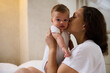 © Taras Grebinets - Cute baby boy looking at camera while his mother cuddling and kissing him