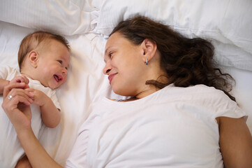 happy young mother lying on the bed with her adorable baby boy 4 months old. mom and kid communicati