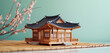 A miniature traditional Korean hanok house with intricate woodwork, on a bamboo mat. The background is a soft mint green.