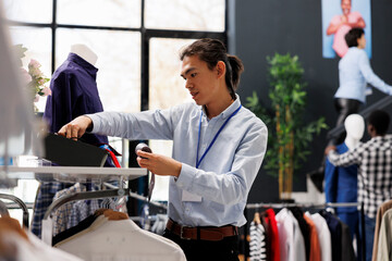 Wall Mural - Asian man checking formal belt on store shelf, arranging stylish accessories in clothing store. Shopping mall worker loooking at with fashionable clothes. Fashion new collection concept