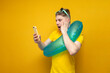 young shocked guy with an inflatable swim ring on vacation in the summer uses a smartphone on a yellow background