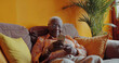 © dreamalittledream - Sophisticated elderly black woman on her phone, relaxing in beautifully design interior with soft cool lighting, architecturally design home, posh home, with short focus portrait shot. Internet.
