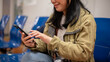 © bongkarn - A female traveler is chatting on her phone while waiting for her boarding time at the airport.
