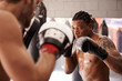 © M Moller/peopleimages.com - Men, coach and martial arts with combat training in fight, gloves and partner for punch at gym. People, challenge and action for mma, boxing and hands with power, workout and exercise for competition