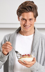 Smile, portrait and man with cereal in kitchen of home for hydration, health and wellness. Happy, confident and young male person eating breakfast with fruit, yoghurt and muesli in modern apartment.