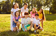 © Studio Romantic - Happy kids in a sunny summer park. Outdoor group portrait of little friends on a green meadow. Several children sitting and standing on a green grassy lawn, looking at the camera and smiling