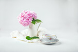 Fototapeta Do pokoju - Still life with a blooming bouquet of pink hydrangea in a vase and a fine porcelain cup of coffee on a white background