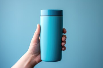 Poster - Hand holding a blue water bottle against a blue background, perfect for hydration concept