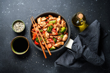 Wall Mural - Chicken stir fry with vegetables and sesame at black background. Traditional asian cuisine.