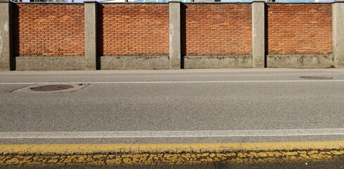 Wall Mural - High surrounding brick wall with concrete columns at the road side. Empty large street in front with road line markings. Urban background for copy space.