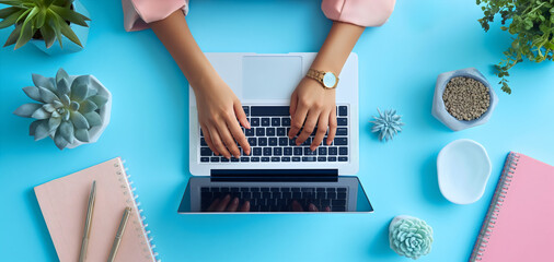 Top view of the businesswoman in a light pink shirt typing with her hands on a laptop or notebook computer device on a blue office desk or table. Employee online job, using technology