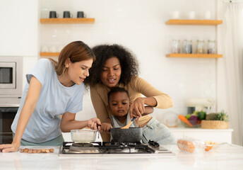 Wall Mural - Multiracial lesbian couple cooking healthy food in kitchen for their biracial child. Beautiful gay women standing at counter enjoy preparing lunch at home with kid. Happy LGBT family eating lifestyle.