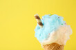 Leinwandbild Motiv Sweet cotton candy in waffle cone on yellow background, closeup. Space for text