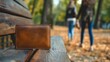 Closeup of a lost brown leather wallet on the wooden bench in a sunny autumn park outdoors. Two women walking away from a money purse, forgetting to pick it up. Left or dropped from the pocket