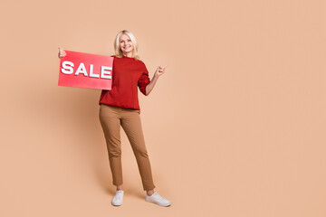 Sticker - Full length photo of pretty cute woman wear red sweater holding sale board showing finger empty space isolated beige color background