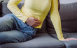 Close up of unknown young woman holding belly sit on sofa at home, feeling discomfort, health problem concept, suffering from stomach ache, food poisoning, gastritis, abdominal pain, menstrual period