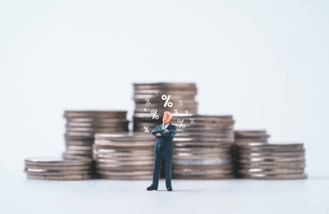 Wall Mural - Businessman miniature figure standing with percentage sign and coins stacking for considering of increase or decrease interest rating to get dividend and profit concept.