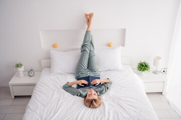 Poster - Full body size photo of blonde hair girl tired reading fiction book lying down cozy bed indoors legs upside relax after long story