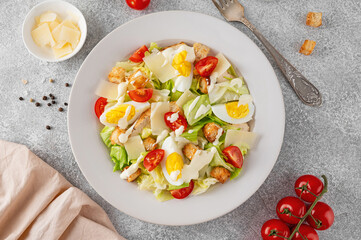 Wall Mural - Caesar salad with lettuce, grilled chicken breast, boiled eggs, tomatoes, parmesan cheese and croutons in a ceramic plate on a concrete background. Top view.