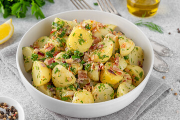 Wall Mural - Warm potato salad with bacon, onion, fresh herbs and vinegar dressing in a bowl on a gray concrete background. German Kartoffelsalat.